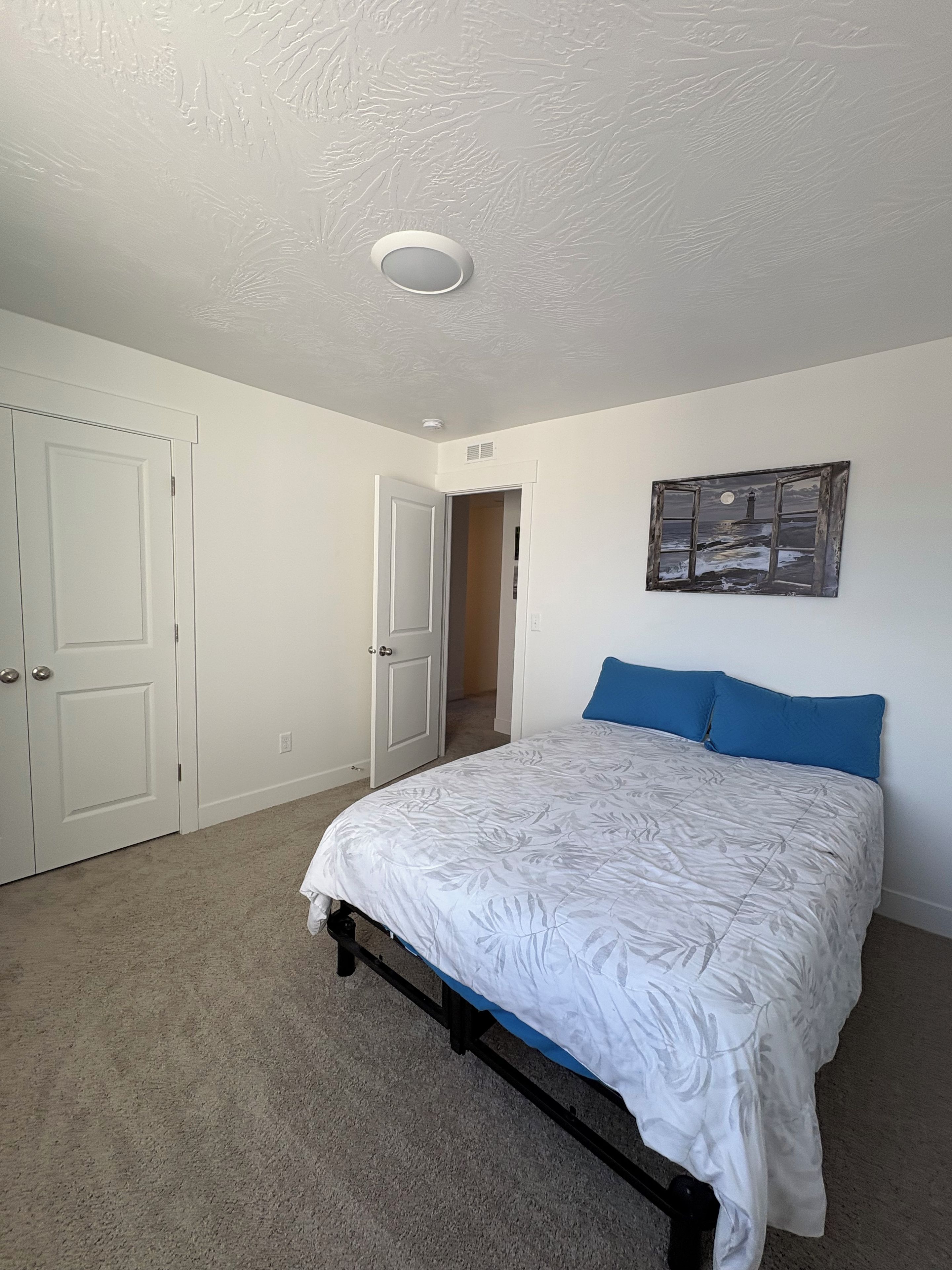 Un dormitorio con cama, una puerta, un pasillo y un cuadro colgado en la pared.