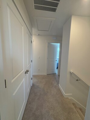 A hallway with carpeted flooring, white walls, and doors leading to other rooms. - New townhome in peaceful- friendly neighborhood with 3 bedrooms and 2.1/2 bath (Eagle Mountain)