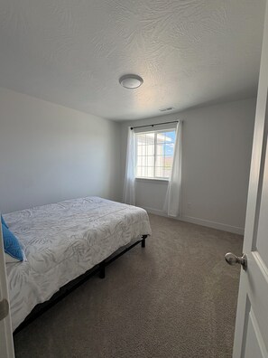 Une chambre avec un lit simple, une fenêtre avec des rideaux blancs et une porte.
