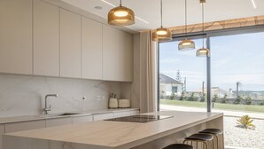 Eine moderne Küche mit Marmorarbeitsplatte, Barhocker, Pendelleuchten und Blick durch große Fenster.
