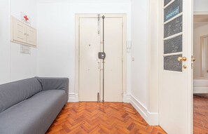 Ein Zimmer mit grauem Sofa, einer weißen Tür mit Schloss, einem Fischgrätenparkett und einem Schild an der Wand.
