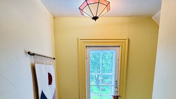 A narrow hallway with a window, a wall-mounted tapestry, and a ceiling light fixture.