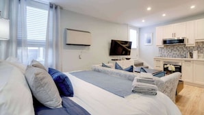 Een moderne hotelkamer met een groot bed, een flatscreen televisie, een kitchenette en een raam met gordijnen.