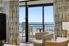 A room with a view of the beach, a chair, a table, and a lamp. - Beach Cove Resort 515 Oceanfront Condo (North Myrtle Beach)