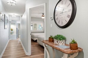 A hallway with a clock, a wooden bench with plants, and a door leading to a bedroom. - Beach Cove Resort 515 Oceanfront Condo (North Myrtle Beach)