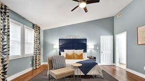 A bedroom with a bed, a chair, a small table, a ceiling fan, and a sign that reads 'EAST ATLANTA'. - Beautiful Den 4Bd 4bth Perfect for Longer Stays (Atlanta)