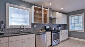 A modern kitchen with white cabinets, a stainless steel dishwasher, a gas stove, and a microwave. - Beautiful Den 4Bd 4bth Perfect for Longer Stays (Atlanta)