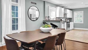 A modern kitchen with white cabinets, a dining area with a wooden table and chairs, and a large mirror on the wall. - Beautiful Den 4Bd 4bth Perfect for Longer Stays (Atlanta)