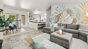 A modern living room with a grey sectional sofa, a coffee table, and a large wall mural. - 6BR Boise Getaway - Arcade - Hot Tub - King Beds - Fire Pit - Sleeps 15+ (Boise)