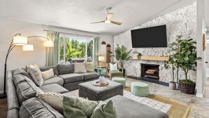 A living room with a sectional sofa, a fireplace, a mounted TV, and a ceiling fan. - 6BR Boise Getaway - Arcade - Hot Tub - King Beds - Fire Pit - Sleeps 15+ (Boise)
