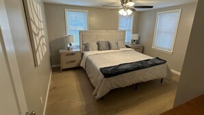 Une chambre à coucher avec un lit, des tables de chevet, un ventilateur de plafond et une fenêtre.