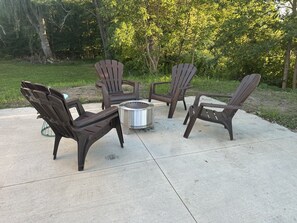 A concrete patio with four Adirondack chairs and a round fire pit.