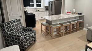 Une cuisine moderne avec un îlot central, des tabourets de bar, un fauteuil à motifs et un coin repas.