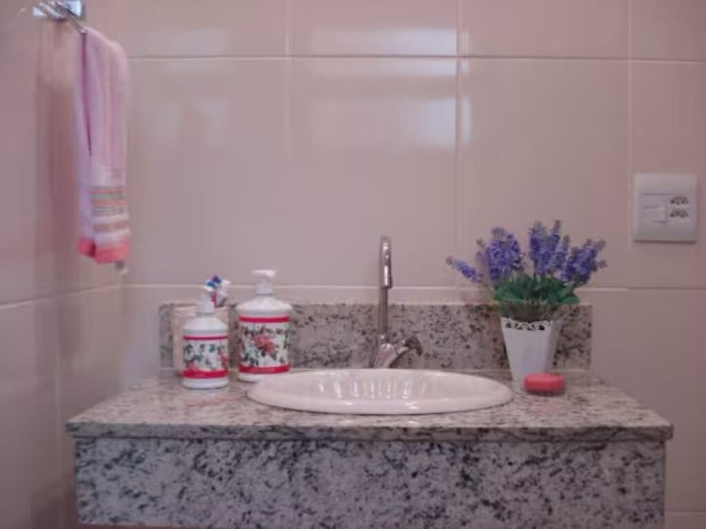 Une salle de bain avec un comptoir en granit, un lavabo blanc, une serviette rose, un distributeur de savon à motifs floraux et un pot de lavande.
