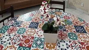 Una sala de estar con un sofá marrón, piso de baldosas, una orquídea en maceta y un cuadro en la pared.