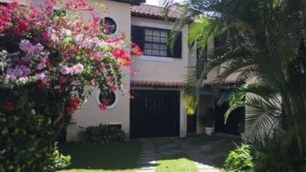 Una casa con entrada pavimentada, un césped pequeño y una palmera.