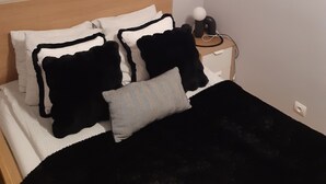 Ein Schlafzimmer mit einem Bett, Kissen, einem Nachttisch mit Lampe und einem Wandbild im abstrakten Stil.
