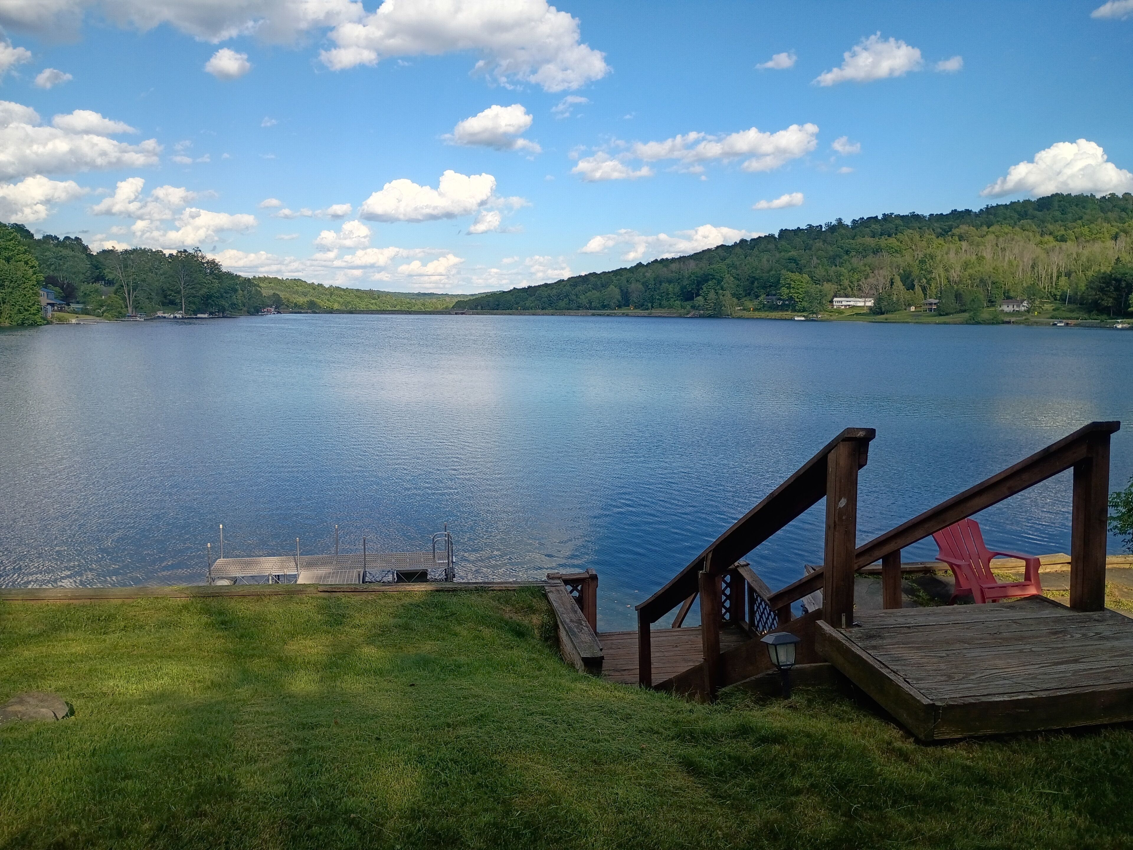 Ein See mit einem Holzsteg und Treppen zu einer Plattform mit einem roten Stuhl.