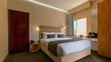 Una habitación de hotel con cama, mesita de noche, lámpara y espejo.