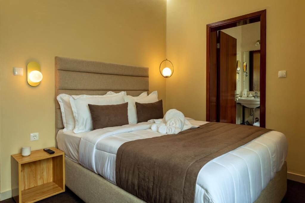 A neatly made bed with a headboard, bedside lamps, and a wooden nightstand with a remote control.