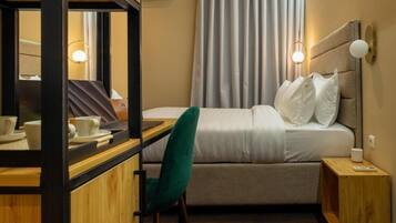 Une chambre d’hôtel comprenant un lit, un bureau avec une chaise, un miroir, une table de chevet et une fenêtre avec des rideaux.