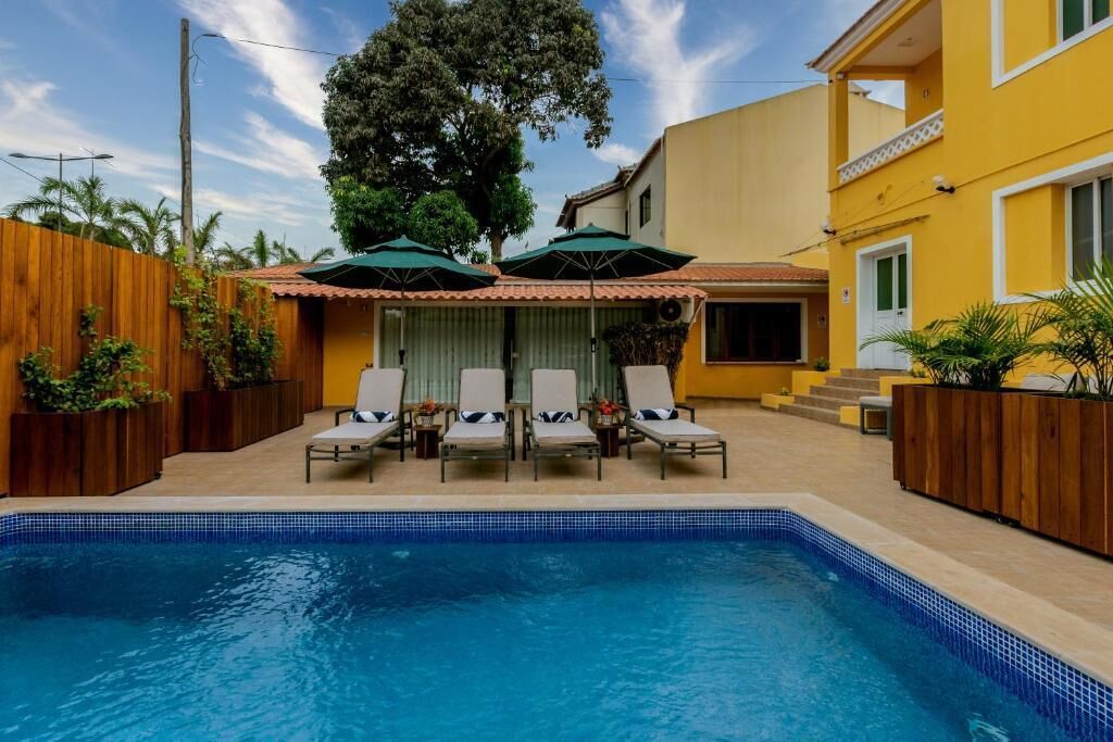A swimming pool with lounge chairs and umbrellas, surrounded by wooden fences and plants.