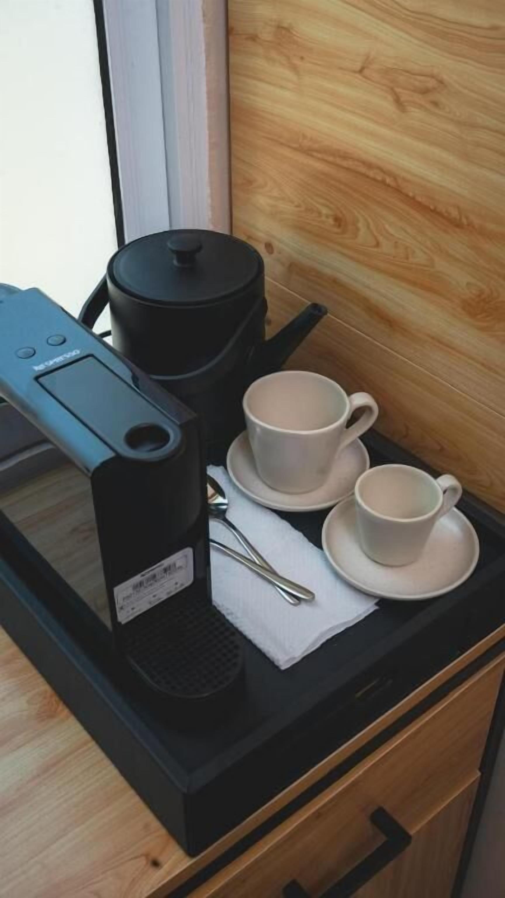 Una encimera de cocina con una cafetera, una olla y dos tazas sobre una bandeja.