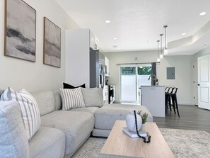 Ein modernes Wohnzimmer mit einem Ecksofa, einem Couchtisch und einer Küchenzeile im Hintergrund.