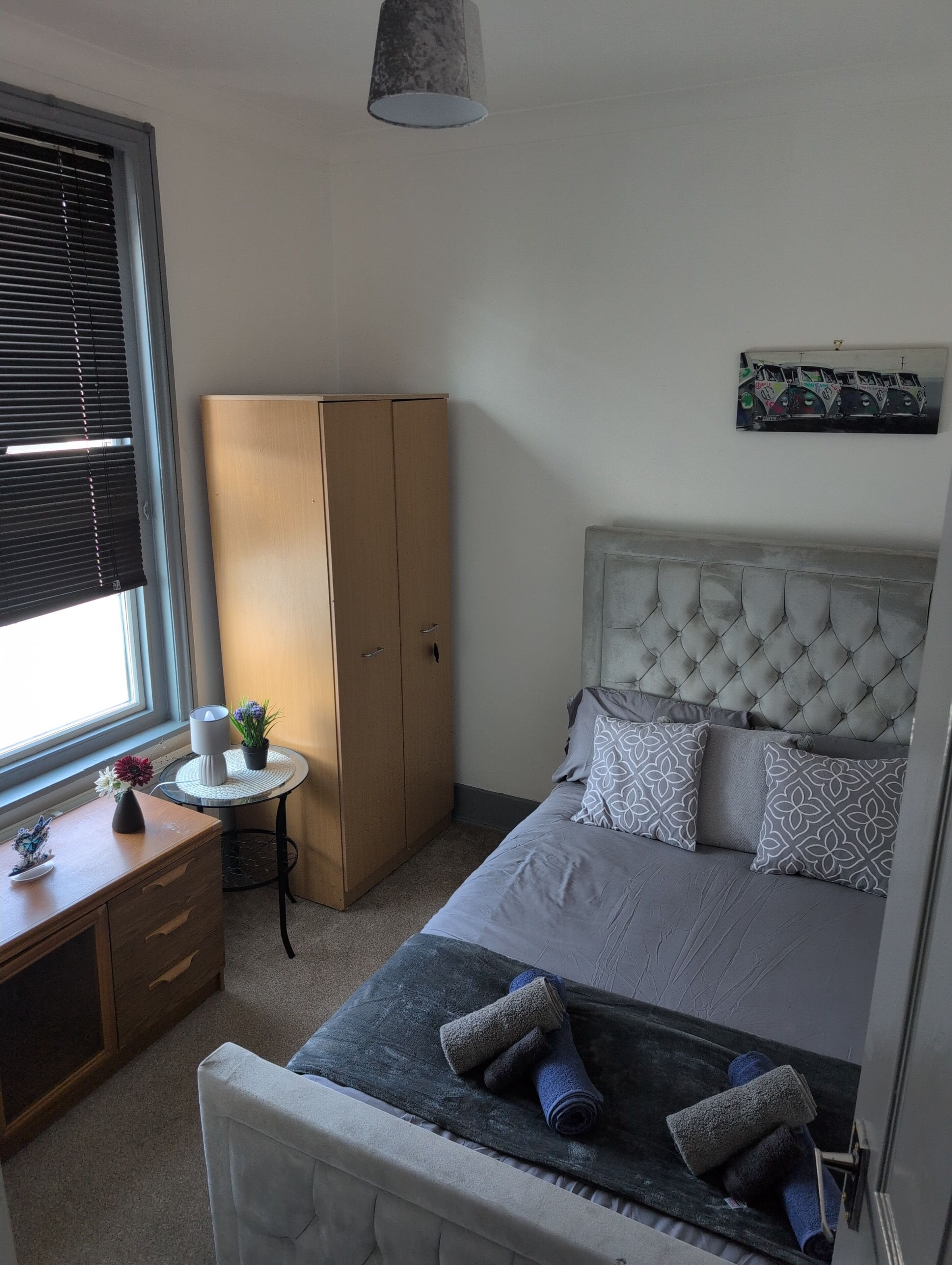 Ein Schlafzimmer mit Bett, Kleiderschrank, Schreibtisch und einem Fenster mit Jalousien.