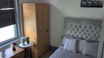Ein Schlafzimmer mit Bett, Kleiderschrank, Schreibtisch und einem Fenster mit Jalousien.