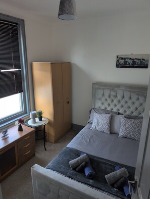 A bedroom with a bed, a wardrobe, a desk, and a window with blinds.