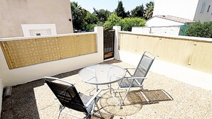 Eine Außenpatio mit einem runden Tisch, zwei Stühlen, einem Tor und einem Gebäude mit Ziegeldach.