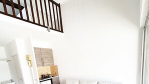 Ein geräumiger Wohnbereich mit einem weißen Sofa, einer Küche mit Herd und einer Treppe.