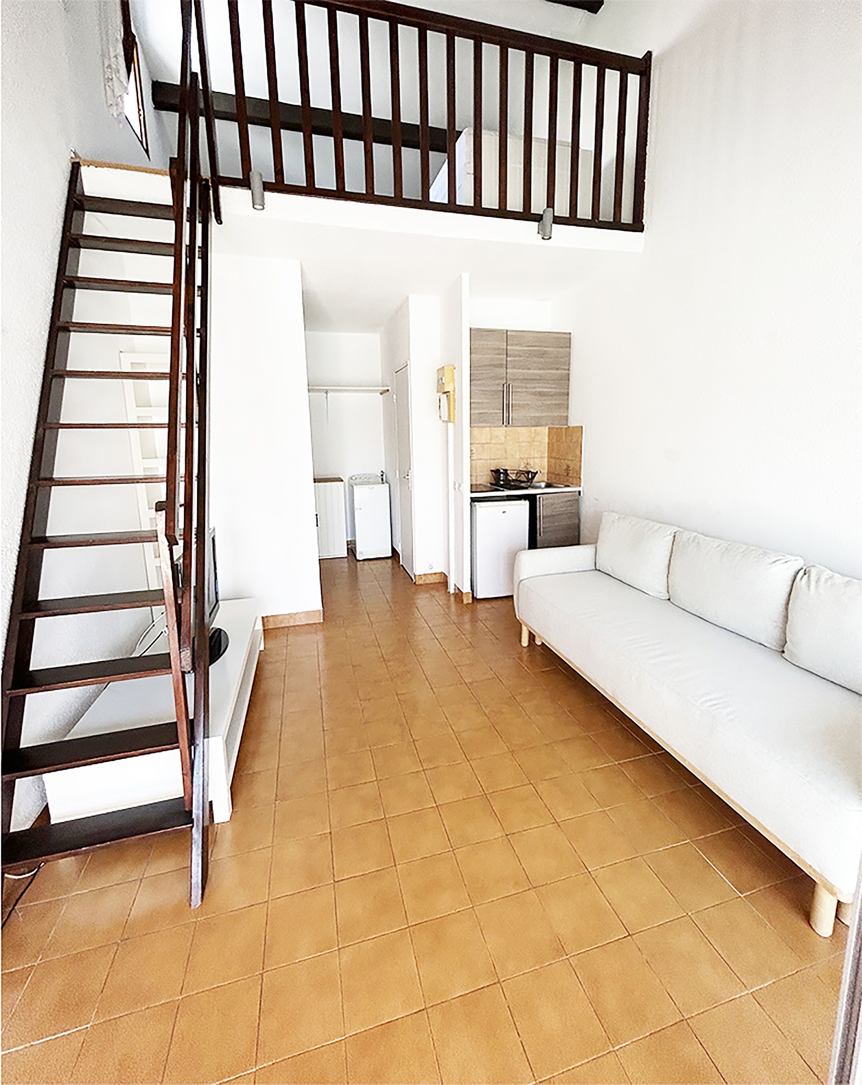 Un vaste espace de vie avec un escalier, un canapé blanc et une cuisine en arrière-plan.