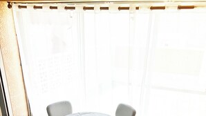 Ein Zimmer mit einem runden Tisch, vier Stühlen, einem Fenster mit Vorhängen und einem Fliesenboden.