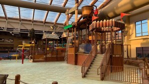 Un parc aquatique intérieur doté d’une aire de jeux en bois, d’un toboggan aquatique et d’un escalier menant à un niveau supérieur.