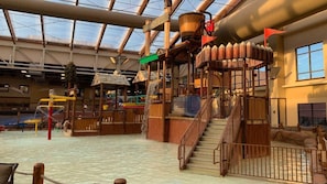 Ein Indoor-Wasserpark mit einem Spielbereich aus Holz, einer Wasserrutsche und einer Treppe zu einer höheren Ebene.