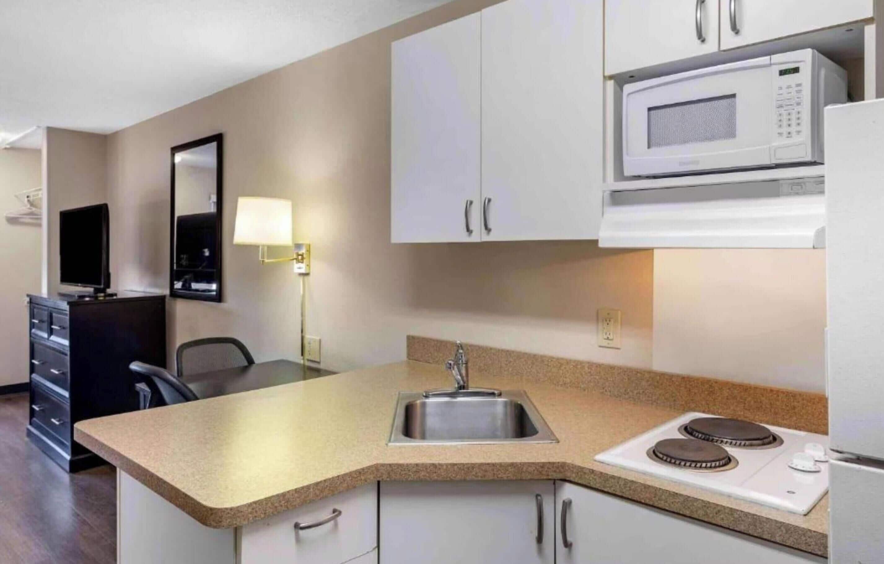 A compact kitchen with a microwave, stove, sink, and a television in the corner.