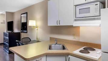 A compact kitchen with a microwave, stove, sink, and a television in the corner.