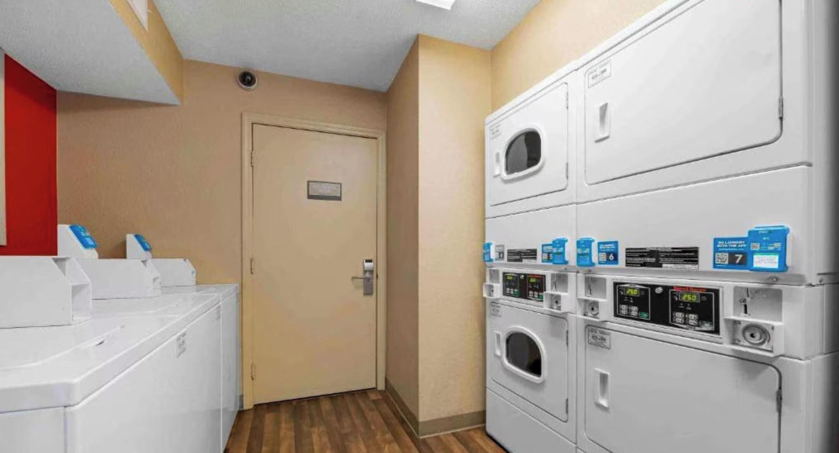 A laundry area with stacked washers and dryers, a door, and a red wall.