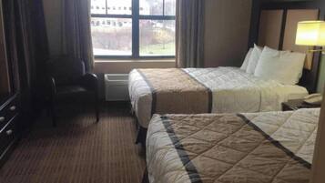 A hotel room with two beds, a chair, a desk, and a window with a view of a building and trees.