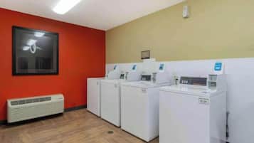 Une buanderie avec quatre machines à laver et quatre sèche-linge blancs, un mur rouge, un luminaire au plafond et une bouche d’aération.