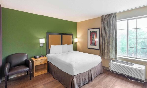 Habitación de hotel con cama, una silla, mesita de noche, ventana con cortinas y un aire acondicionado.