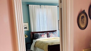 A bedroom with a bed, a window with curtains, a bedside table, a lamp, and a framed picture on the wall.