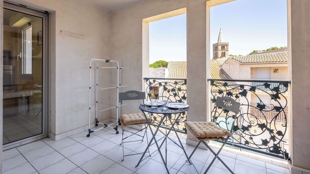 Un balcon avec une table, des chaises et un étagère en métal.