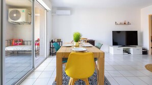 Un salon moderne comprenant une table à manger, une chaise jaune, un téléviseur et une porte-fenêtre coulissante donnant sur un balcon.