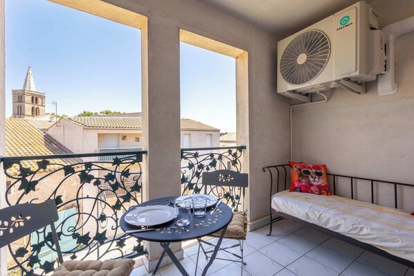 Un balcon avec une table préparée pour deux personnes, un lit agrémenté d’un coussin décoratif et un appareil de climatisation.