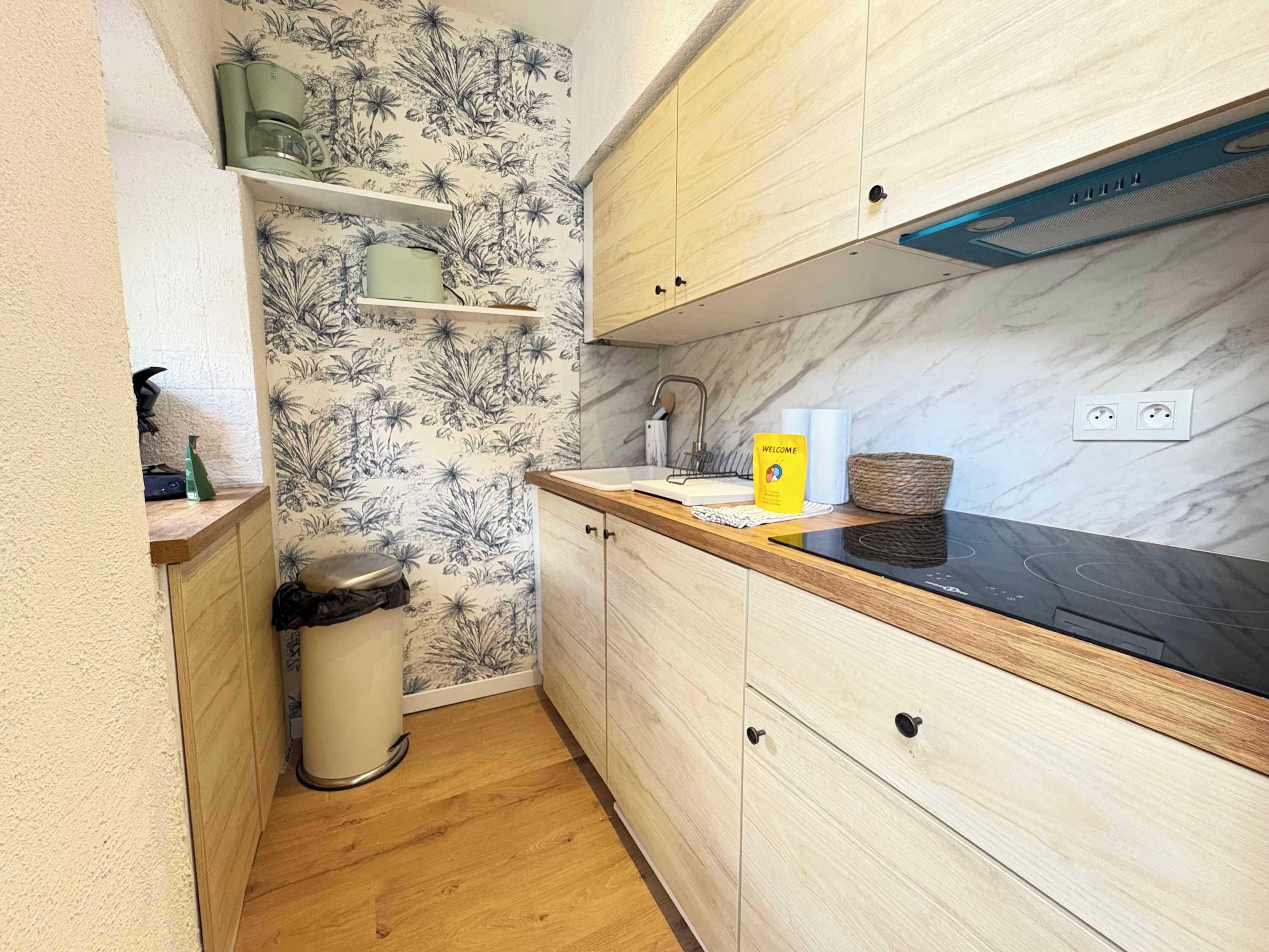 A compact kitchen with wooden cabinets, a marble backsplash, and a small trash bin.