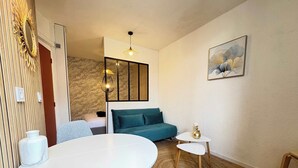 A compact living space with a round dining table, a teal sofa, a small white table, and a woven rug. - Cozy Studio – Seaside Escape by the Water (Agde)