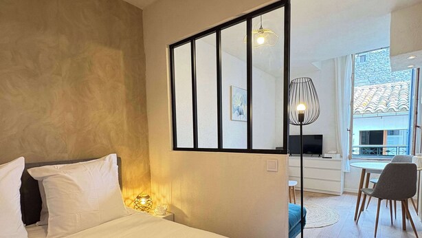 A hotel room with a large bed, a desk, a chair, and a view of the outside. - Cozy Studio – Seaside Escape by the Water (Agde)